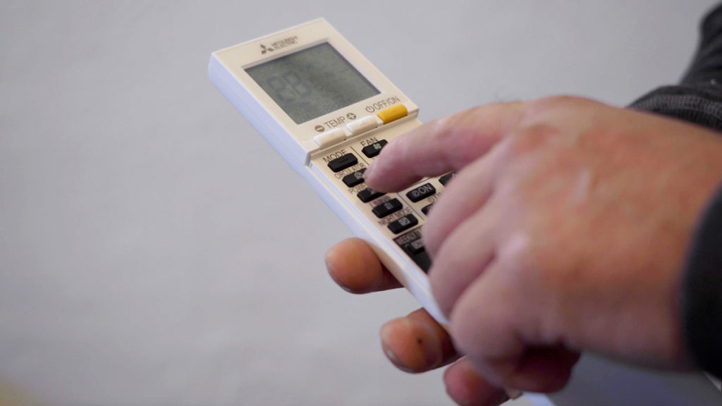 Hånd som trykker på fjernkontroll til varmepumpe. Foto.