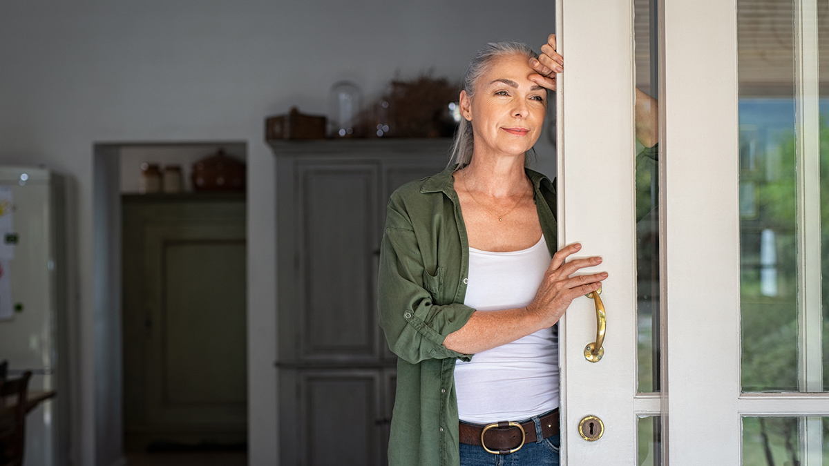 Kvinne ved terrassedør, står og titter ut. Foto.