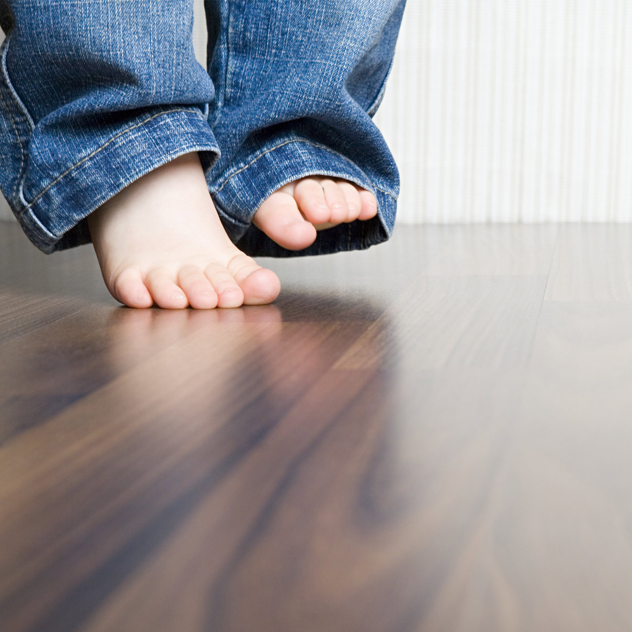 Bare barneføtter på parkettgulv. Foto.