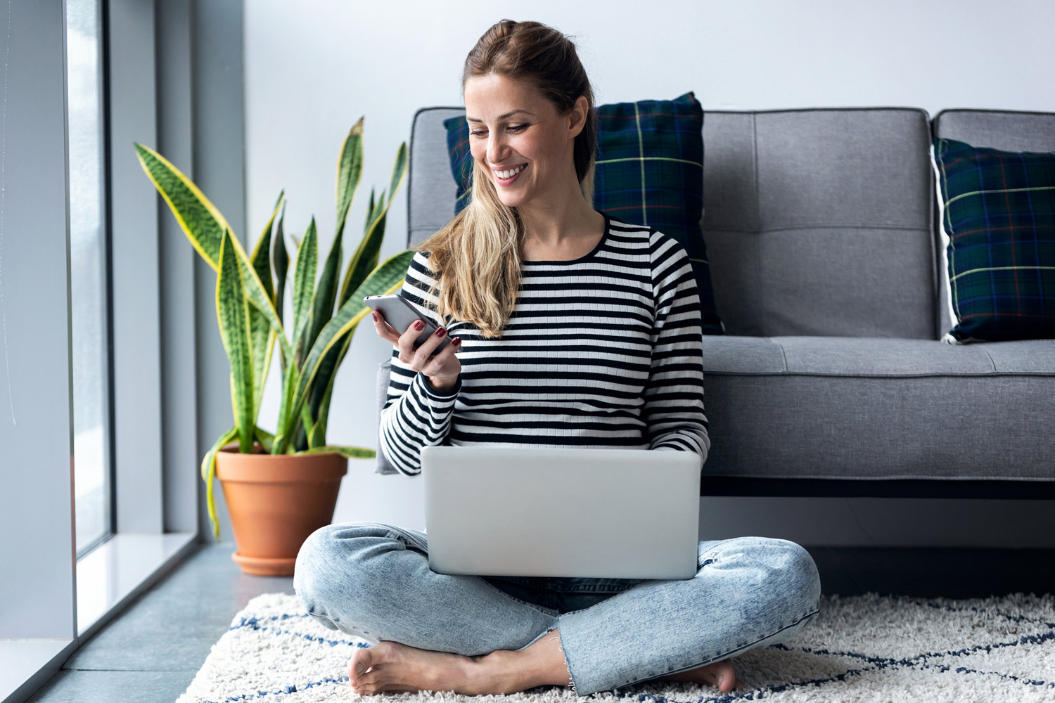 Dame som sitter med pc og mobiltelefon. Foto.