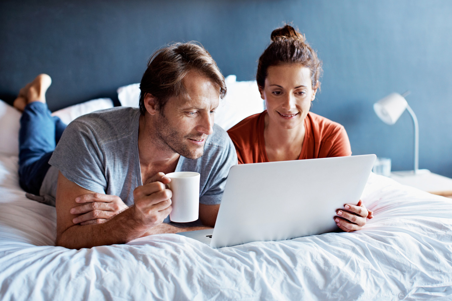Par på sengen med PC foran seg. Foto.