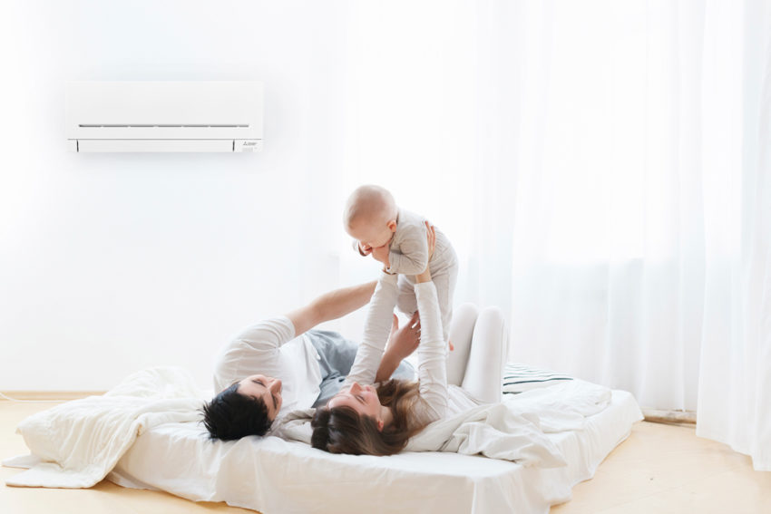 Familie med barn som ligger på madrass . Foto. med en varmepumpe på veggen over dem