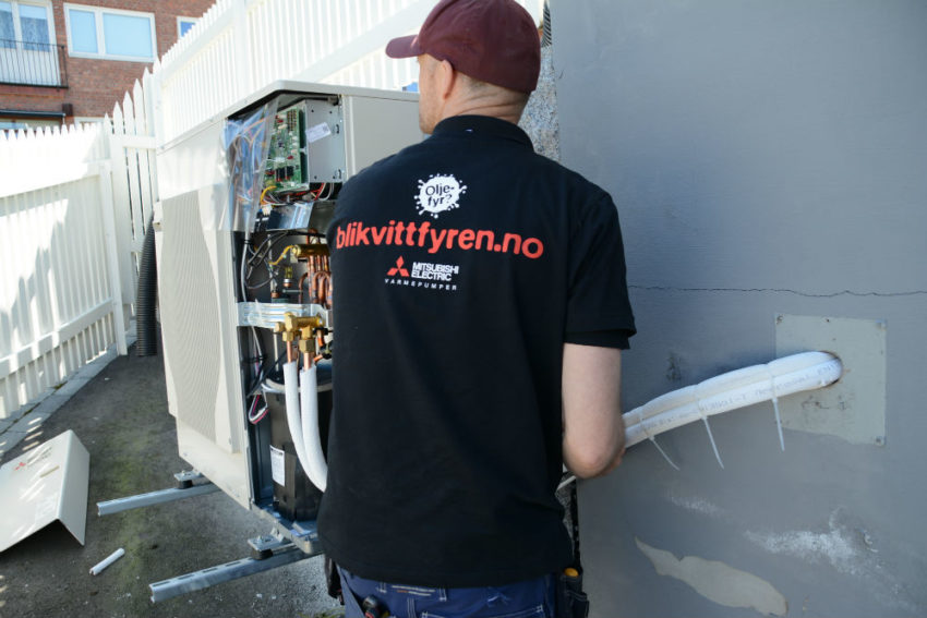 Montør monterer varmepumpe ute. Foto.