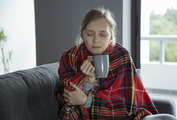 Dame varmer seg med pledd og tekopp. Foto.