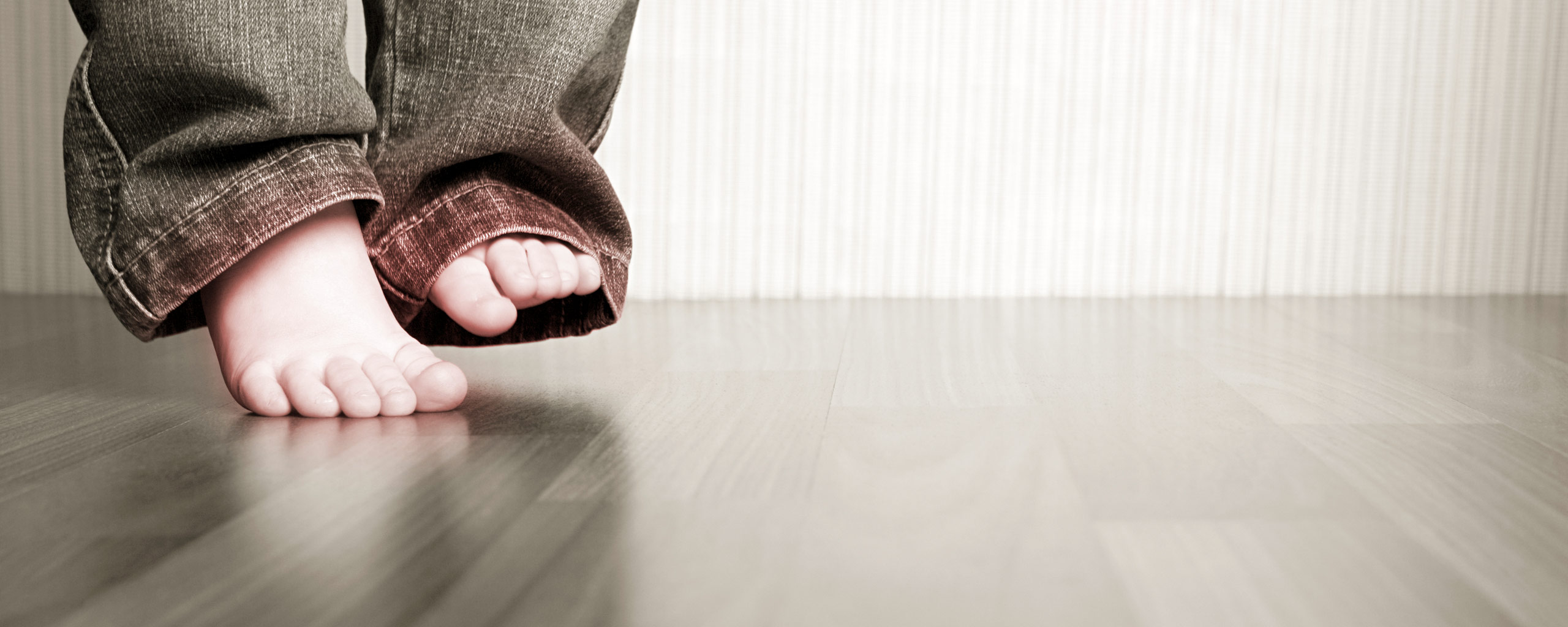 Barneføtter på parkettgulv. Foto.