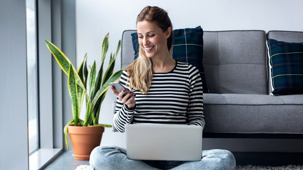 Kvinne ved pc og mobil. Foto