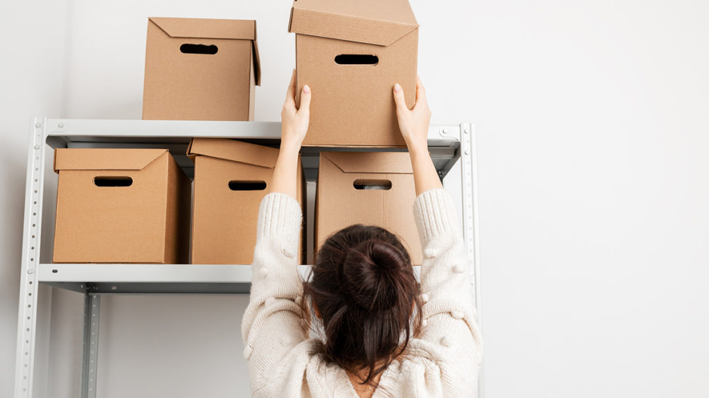 Dame som setter esker i reol. Foto.