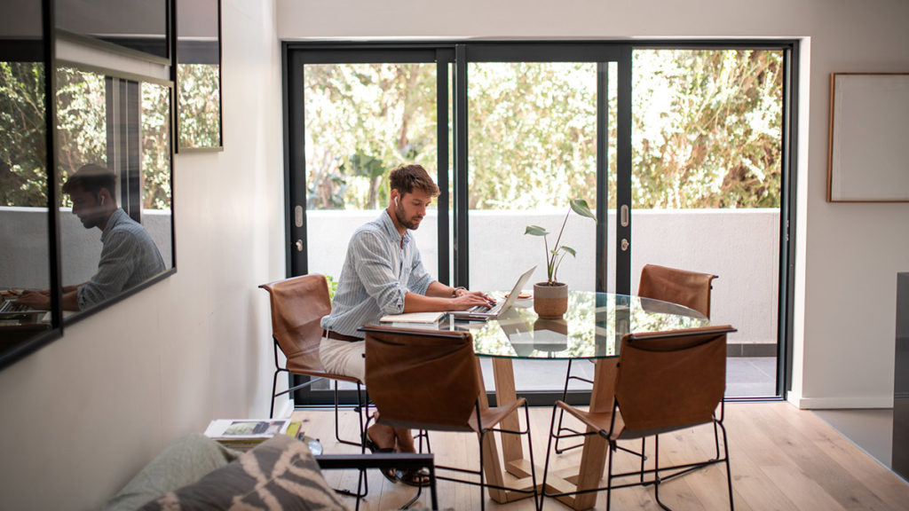 Mann som sitter med laptop ved kjøkkenbordet. Foto.