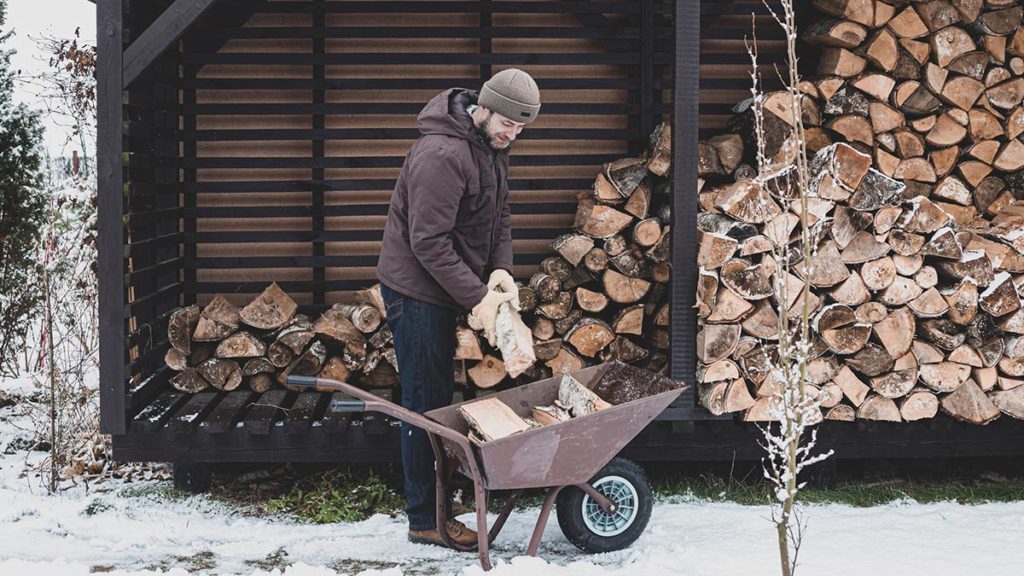 Mann som legger vedkubber i trillebåren. Foto.