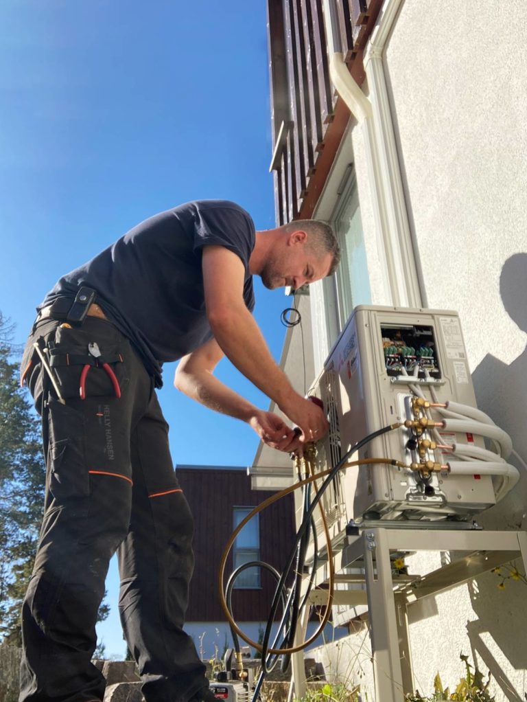 Mann som monterer varmepumpe ute. Foto.